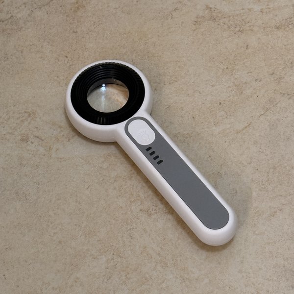 Handheld 60X UV+LED hand lens on a cream limestone counter, white body with a grey grip strip and an LED indicator button on the handle
