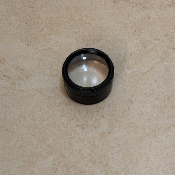 Rongon 30X pocket loupe photographed top-down, a short black cylindrical unit with a textured barrel and a single lens element