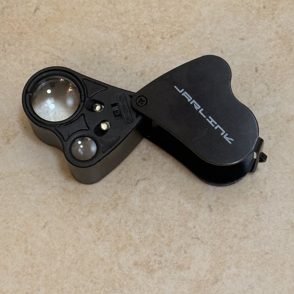JARLINK 30X 60X illuminated folding loupe shown open flat with the black plastic cover swung to one side, revealing two small lens elements and two LED beads inside the barrel