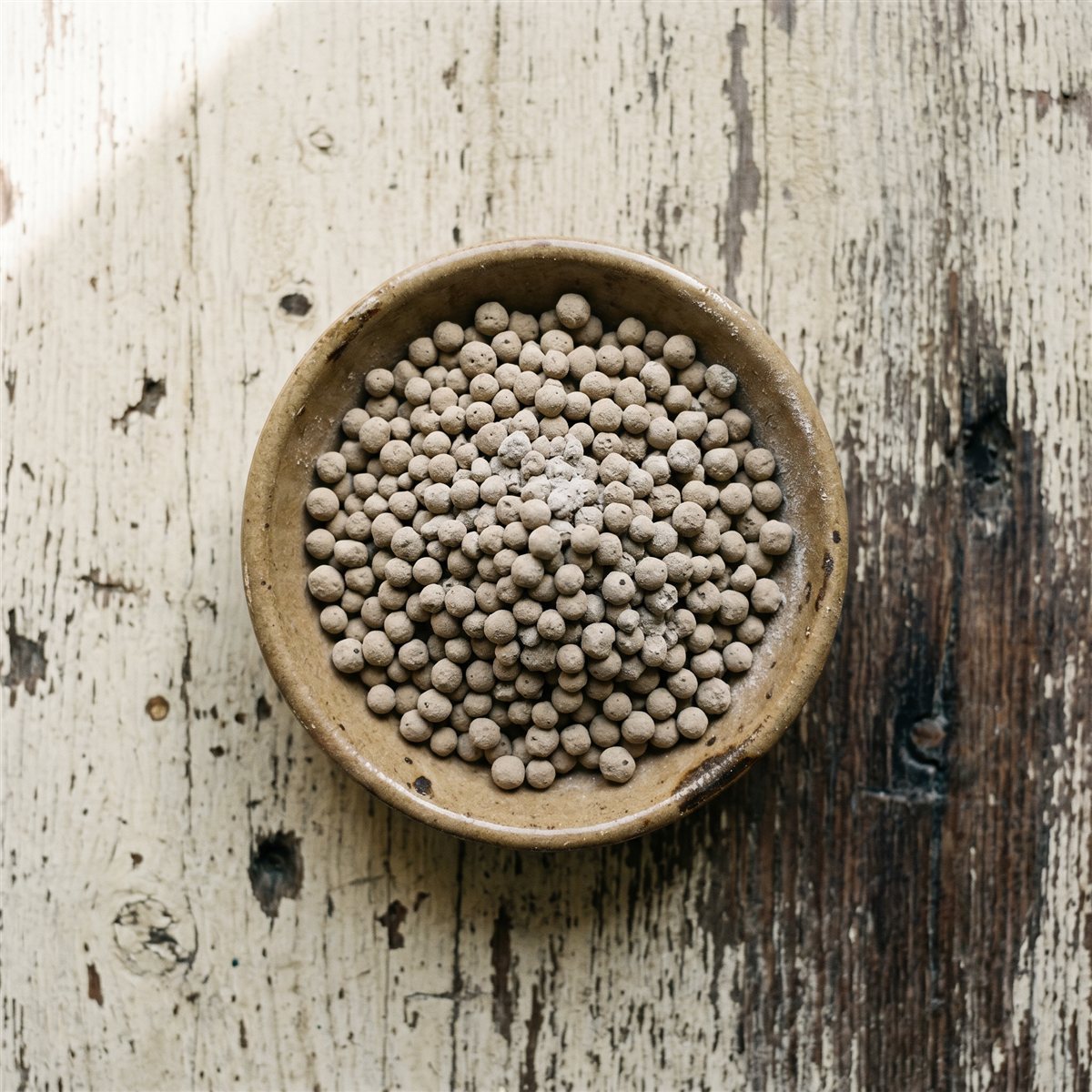 Calcined clay granules in a ceramic bowl on a weathered wood surface